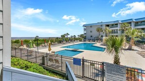 A pool area with two pools, lounge chairs, and a building with balconies. - Unwind by the Beach - Savannah/Tybee (Tybee Island)