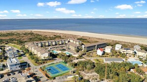An aerial view of a coastal hotel with multiple buildings, a beach, and a tennis court. - Unwind by the Beach - Savannah/Tybee (Tybee Island)
