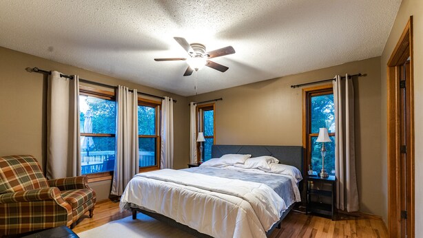 Quarto com cama, poltrona, mesa de cabeceira e ventilador de teto.