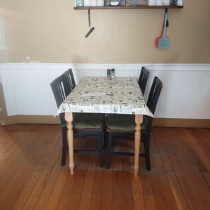 Una mesa de comedor con mantel estampado como periódico, cuatro sillas y un estante fijado a la pared.