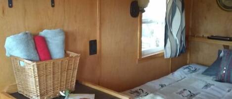 Un dormitorio pequeño con cama, una mesita, una cesta y una estantería.