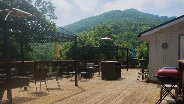 A wooden deck with outdoor furniture, a barbecue grill, and a view of a forested hill.