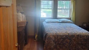 A bedroom with a bed, a nightstand, a lamp, a window with curtains, and a door with a sign.