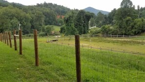 A fenced field with a road running through it, surrounded by trees and hills.