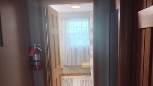A hallway leading to a bathroom with a toilet, a small stool, and a window with curtains.