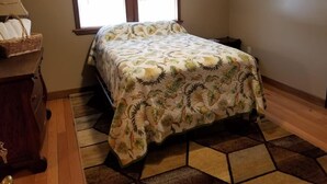 A bedroom with a bed, a window, a wooden dresser, and a patterned rug.