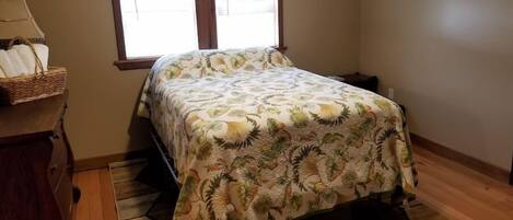 A bedroom with a bed, a window, a wooden dresser, and a patterned rug.