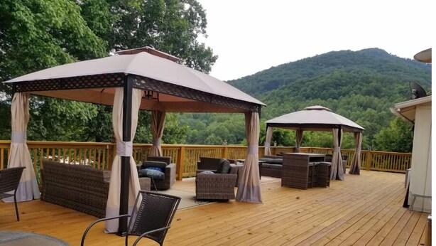A wooden deck with outdoor furniture, including sofas and chairs, and two gazebos providing shade.