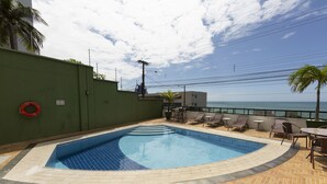 A swimming pool with a tiled deck, lounge chairs, and a view of the sea. - Acorde com vista mar em Ponta Negra (Natal)