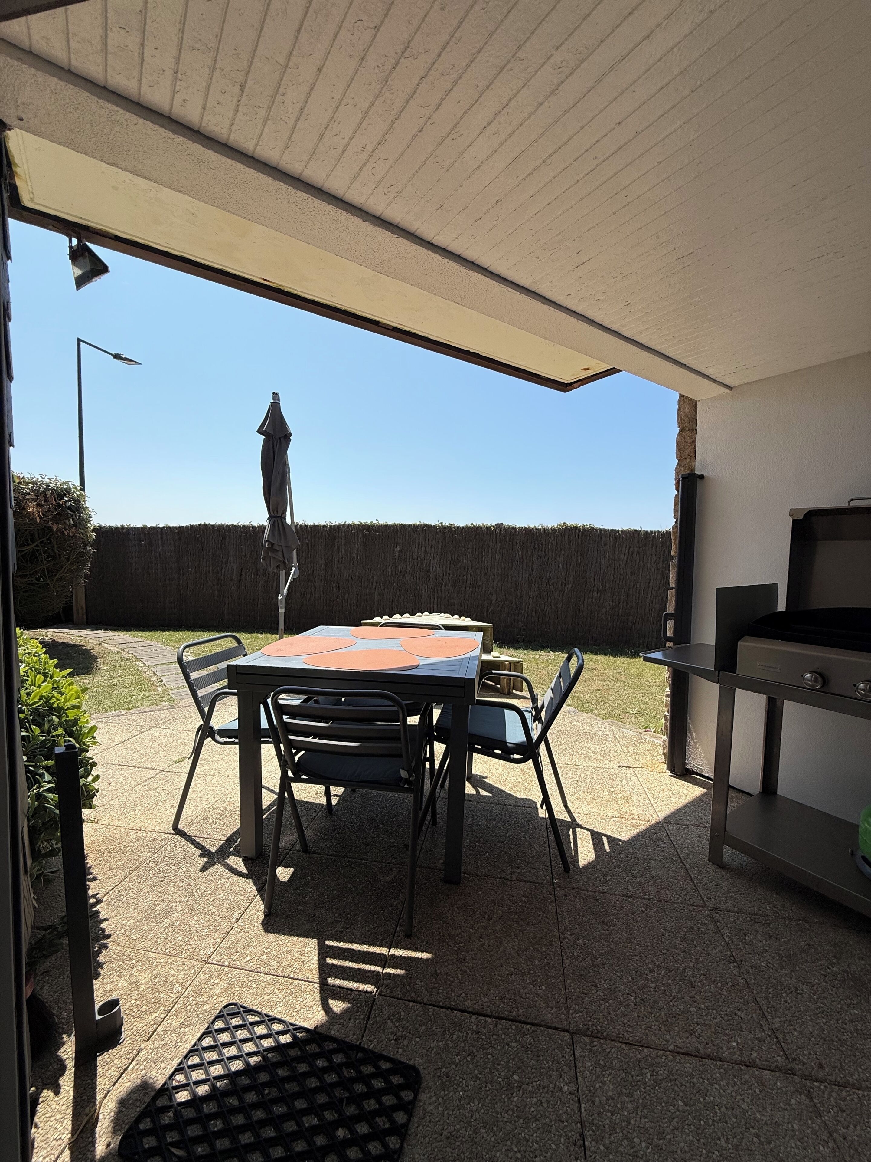 Un patio al aire libre con una mesa y sillas, una parrilla y vistas a un seto y al cielo.