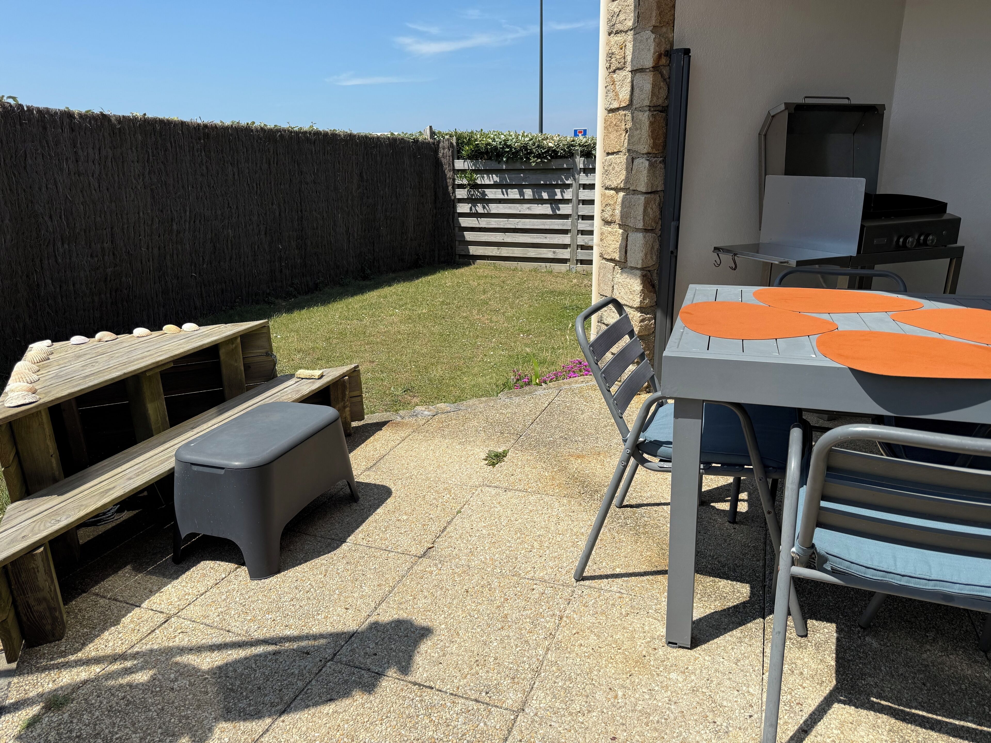 Un patio con mesa y sillas, un banco de madera y una parrilla.