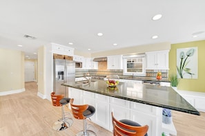 A modern kitchen with white cabinets, a central island with stools, stainless steel appliances, and a decorative bowl of fruit. - Newport Beach Gem with A/C and Two Rooftop Decks (Newport Beach)