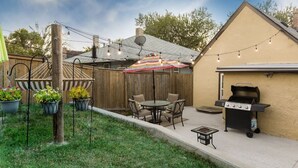 A backyard with a wooden fence, a barbecue grill, a table with chairs, and string lights. - Cozy Apartment Minutes from Downtown (Rapid City)
