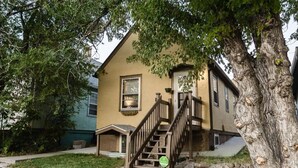 A two-story house with a wooden staircase leading to a front door, surrounded by a stone wall and a large tree. - Cozy Apartment Minutes from Downtown (Rapid City)