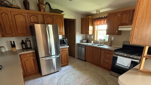 A compact kitchen with wooden cabinets, a stainless steel refrigerator, a microwave, a dishwasher, and a stove. - A Fisherman's Paradise (Harrold)