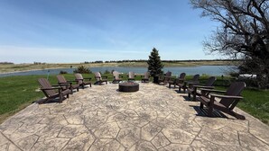 An outdoor seating area with Adirondack chairs and a fire pit, overlooking a lake. - A Fisherman's Paradise (Harrold)