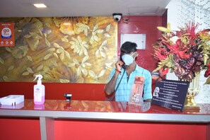 A hotel reception desk with a floral wall mural, a security camera, and a sign about Million Day stays. - Hotel Million Day (Mayiladuthurai)