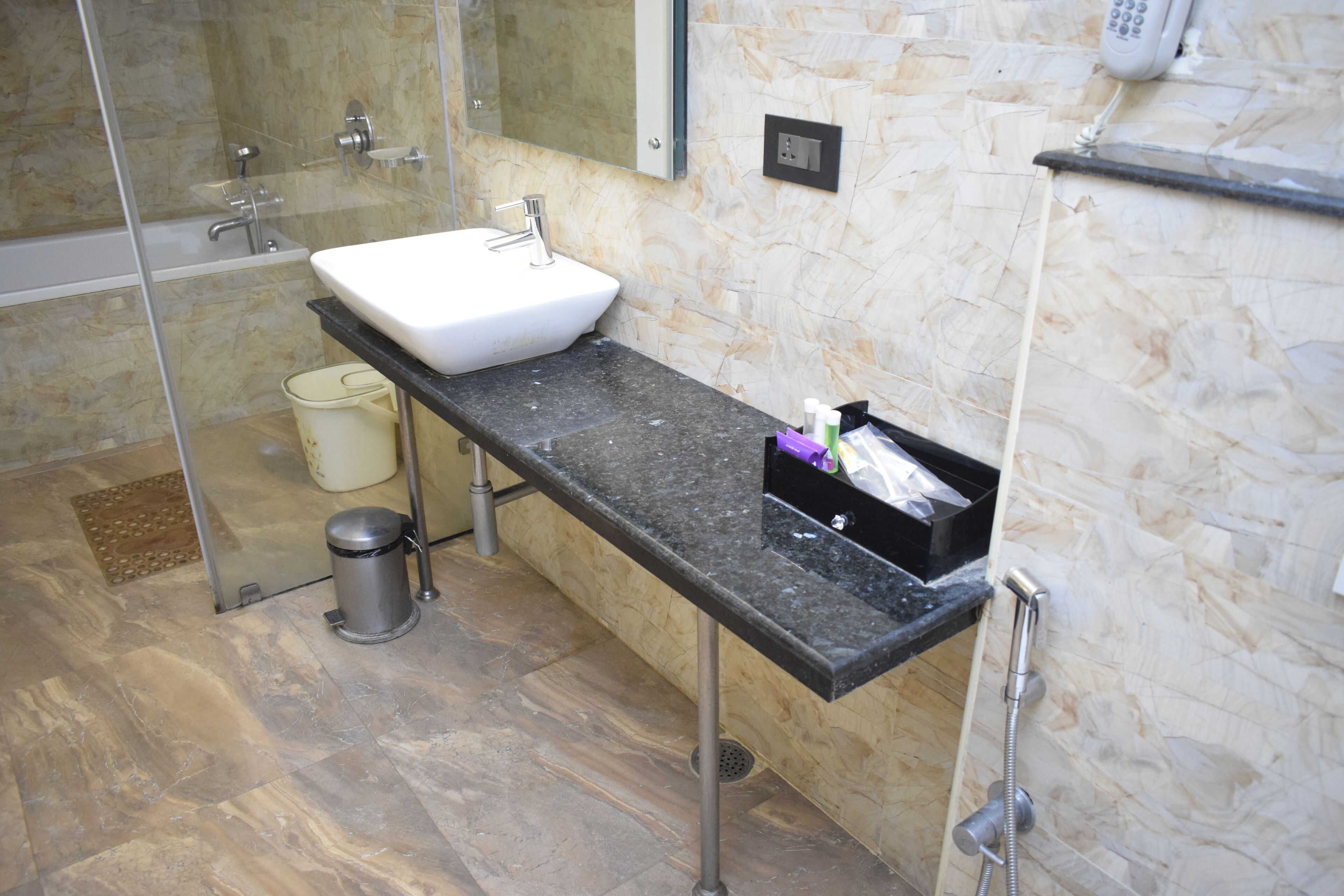 A modern bathroom with a white sink, a black countertop, a glass shower enclosure, and a marble wall.