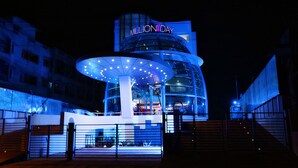 Un hotel moderno con un llamativo letrero 'MillionDay', un amplio dosel circular en la entrada y un acceso mediante portón.