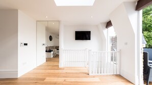Une pièce spacieuse dotée d’un plancher en bois, d’une rambarde blanche et d’un téléviseur à écran plat fixé au mur.