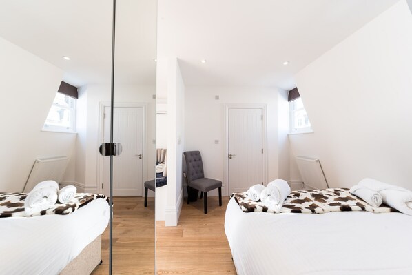 Ein Zimmer mit Spiegel, zwei Betten, einem Sessel und einem Fenster.