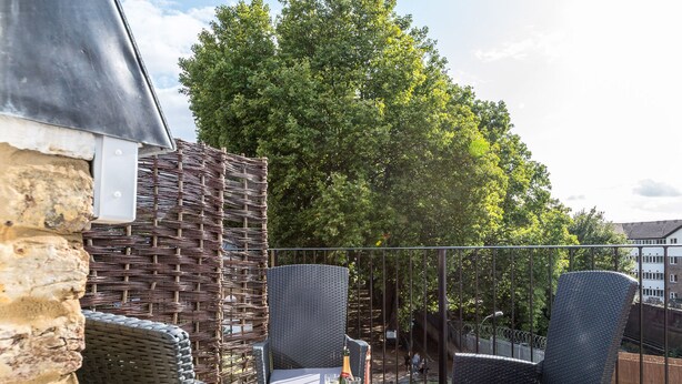A balcony with wicker furniture, a table with a bottle and glasses, and a stone wall. - Pet-friendly Fulham Broadway Penthouse, Sw Balcony (London)