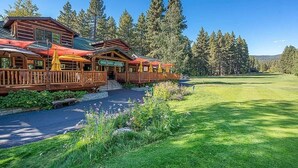 A lodge with a wooden exterior, a covered deck with umbrellas, and a view of a golf course.
