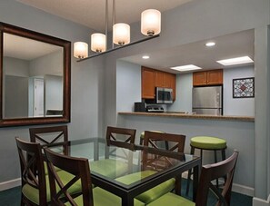 Modern kitchen with microwave and stainless steel refrigerator, wooden cabinets, and dining area with four chairs.