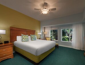 Relax in comfort with a large bed, nightstand, and table, surrounded by a large window and ceiling fan.