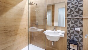 Een moderne badkamer met een houten vloer, een glazen douchecabine, een witte wastafel en een spiegel.