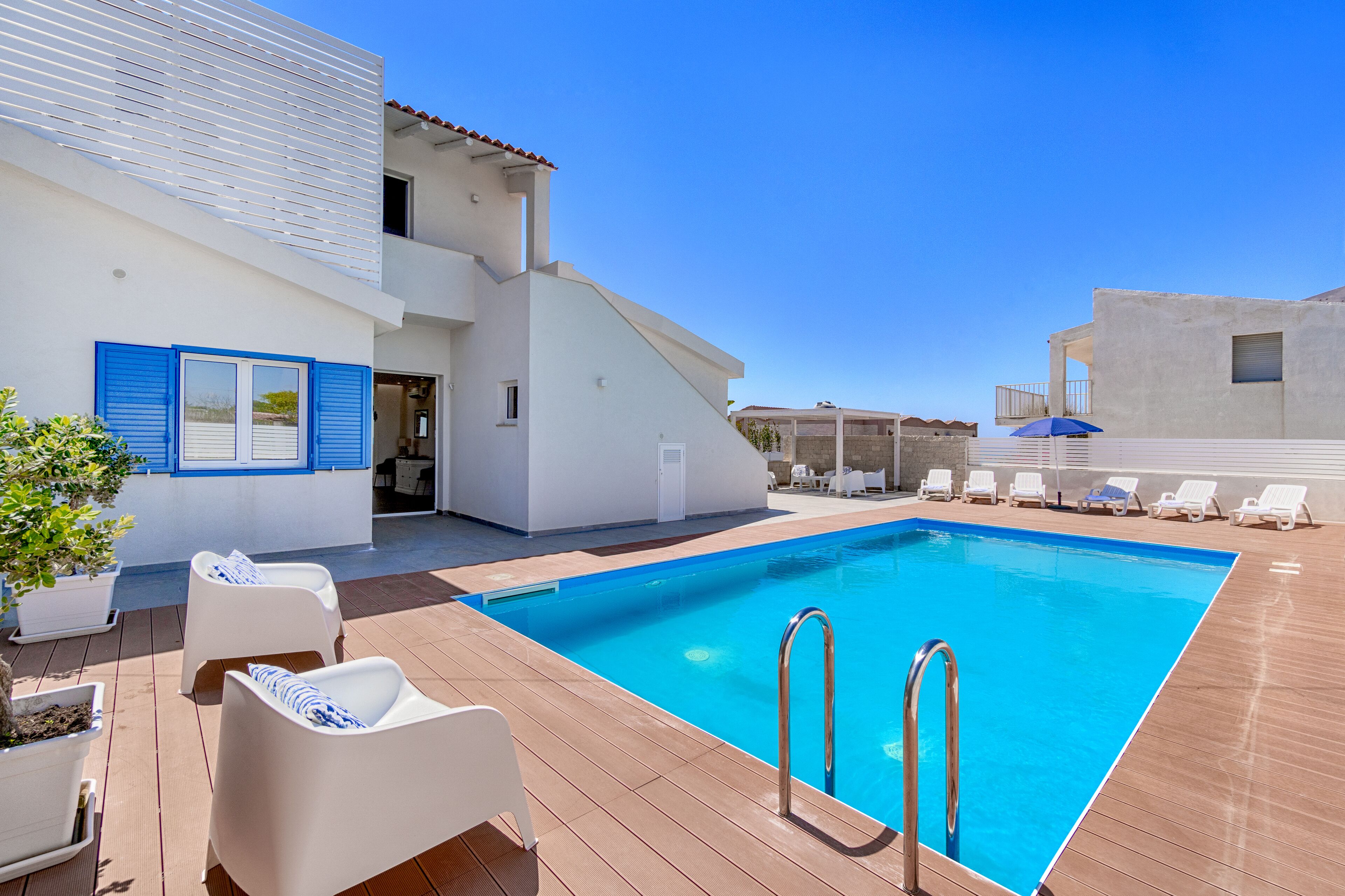 A pool area with lounge chairs, a pool, and a building with blue shutters.