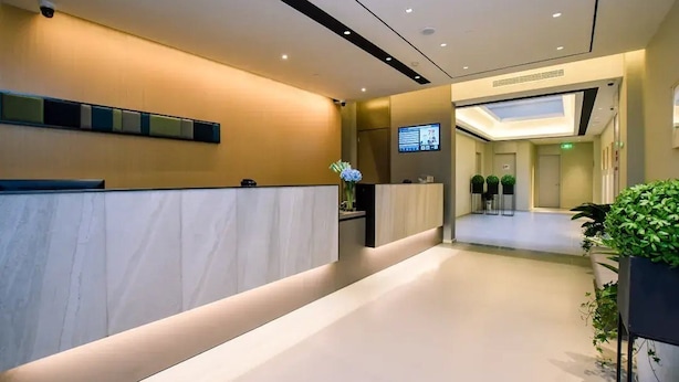 A modern reception area with a reception desk, a digital screen, and a seating area with plants. - Home Inn Selected (Nanjing)