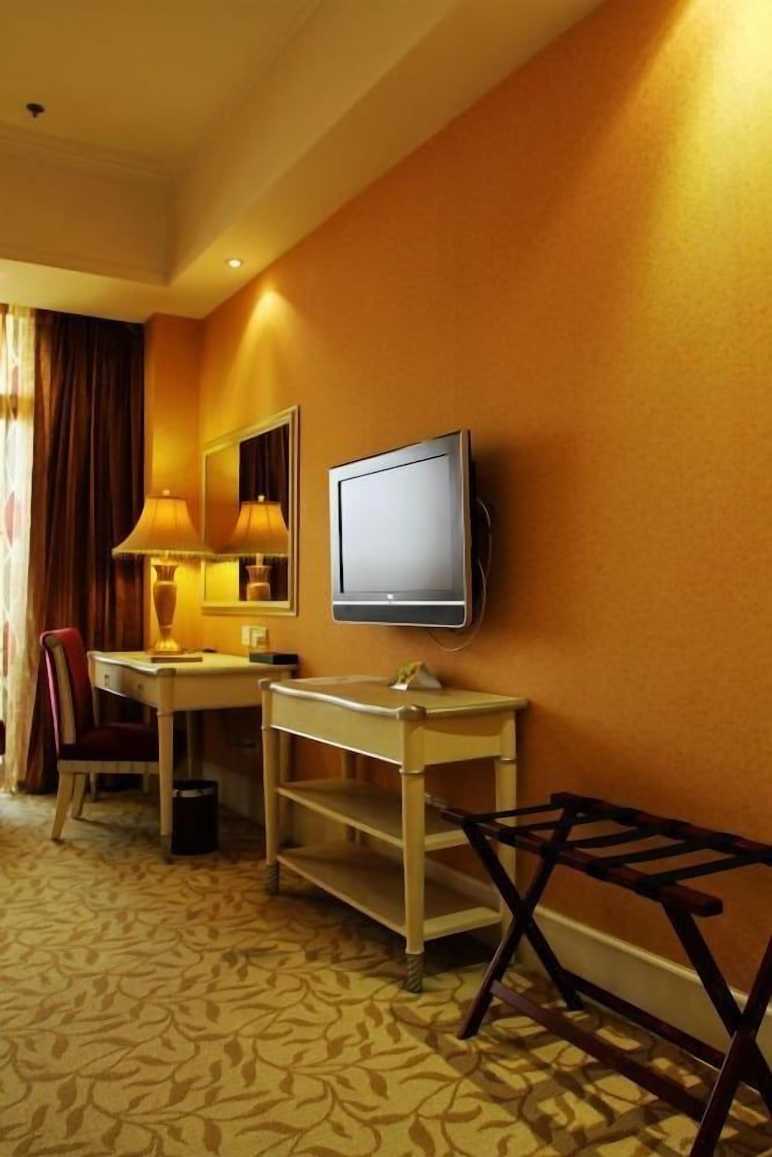 A hotel room with a bed, a desk, a chair, a television, and a lamp.