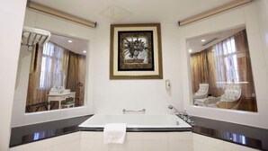 A modern bathroom with a large bathtub, a framed artwork above the tub, and a mirror reflecting a seating area. - Nanjing Suning Universal Hotel (Nanjing)
