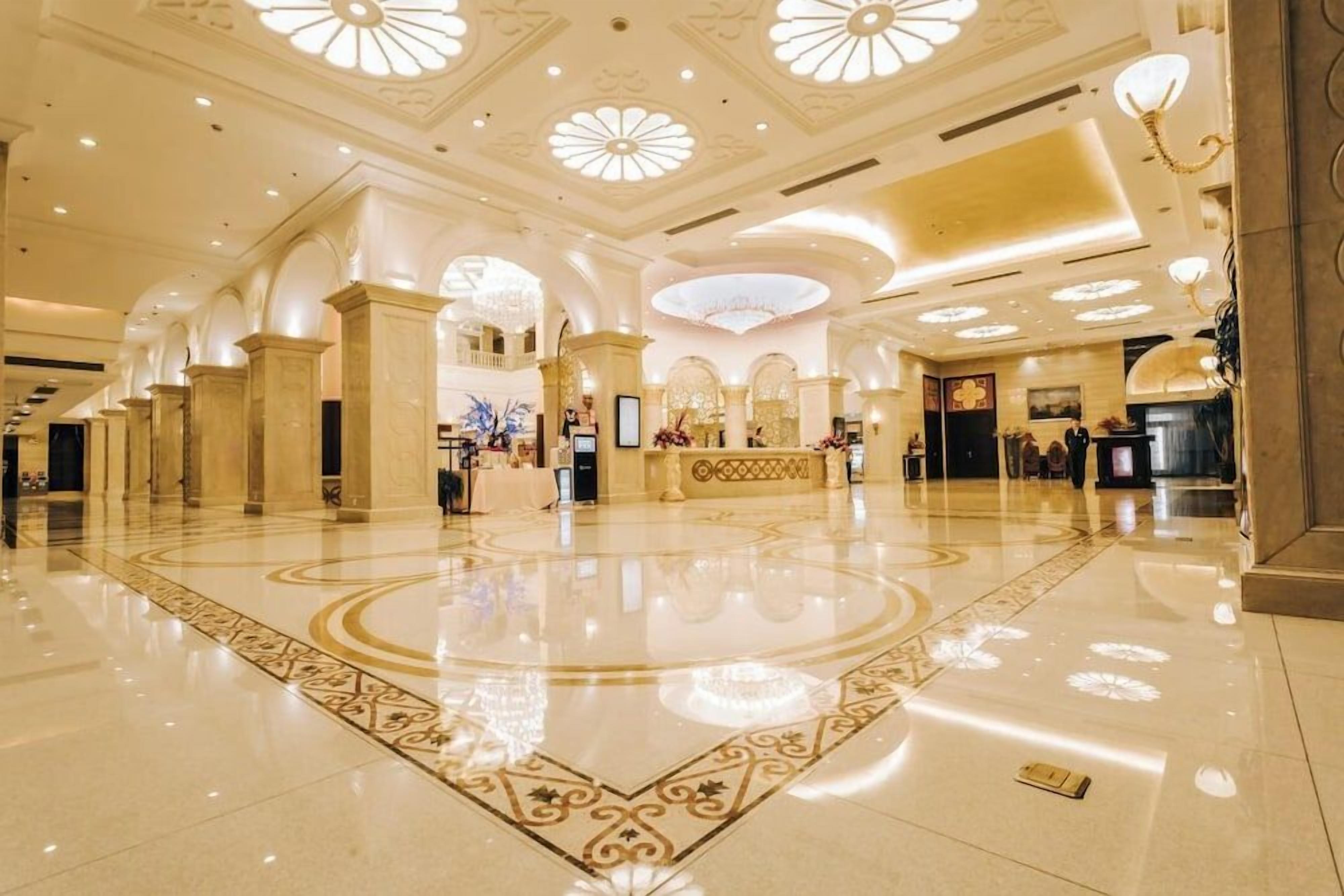 A spacious lobby with a polished floor, ornate ceiling designs, and a reception area.