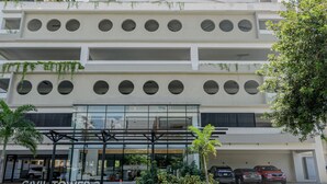 A modern building with multiple floors, large windows, and a parking area with cars. - Amazing Harmony Apt 17FLR in LaJulia @Pool*Gym*Spa (Santo Domingo)