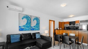 A modern living room with a black leather sofa, a dining table with chairs, and a kitchen area with wooden cabinets and appliances. - Amazing Harmony Apt 17FLR in LaJulia @Pool*Gym*Spa (Santo Domingo)