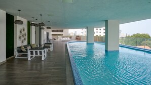 An indoor swimming pool with lounge chairs and a ceiling with hanging lights. - Amazing Harmony Apt 17FLR in LaJulia @Pool*Gym*Spa (Santo Domingo)