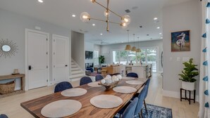 Un vaste espace dédié à la salle à manger, avec une longue table en bois, des chaises bleues et un lustre moderne.