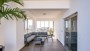 A modern balcony with a grey sofa, two chairs, and a small table.