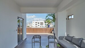 A modern living room with a sofa, two chairs, a table, and a view of a building through a glass door.