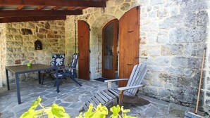 Een terras van stenen met een tafel en stoelen, houten deuren en een stenen muur.