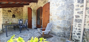 Une terrasse en pierre avec une table et des chaises, des portes en bois et un mur en pierre.