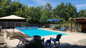 Een rechthoekig zwembad met betegeld zonnedek, omringd door ligbedden en een pergola met een blauwe parasol.