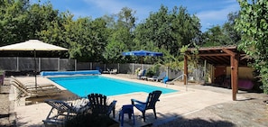 Une piscine rectangulaire avec une terrasse carrelée, entourée de chaises longues et d’une pergola.
