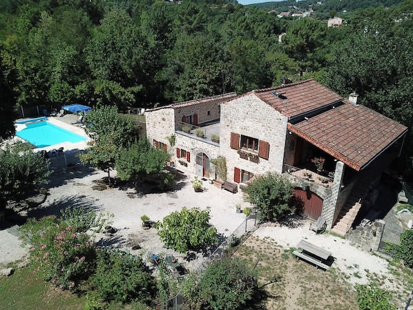 Une maison en pierre avec une piscine, entourée d’arbres et dotée d’une allée gravillonnée.