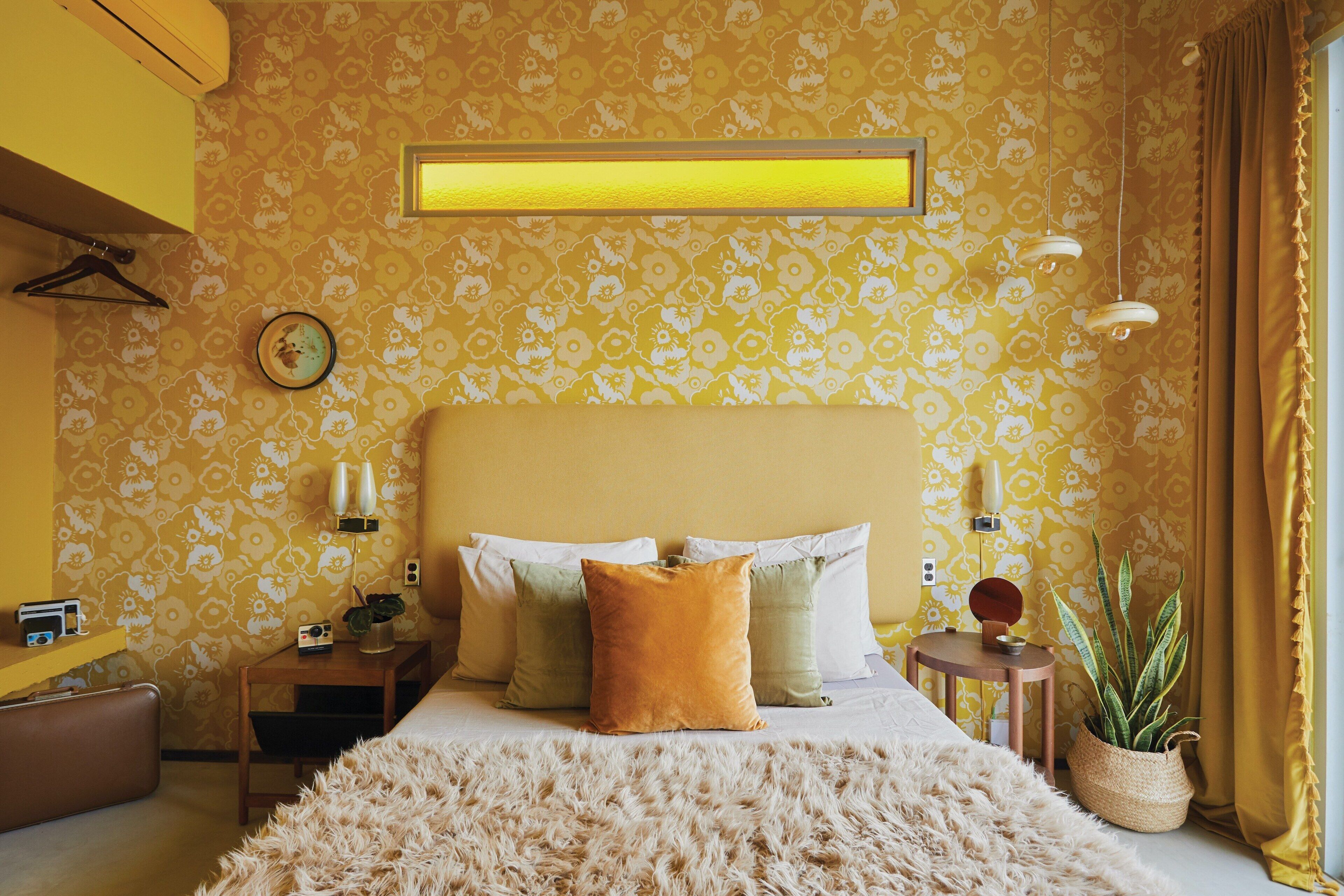 Un dormitorio con cama, mesitas de noche, lámpara, reloj y planta.