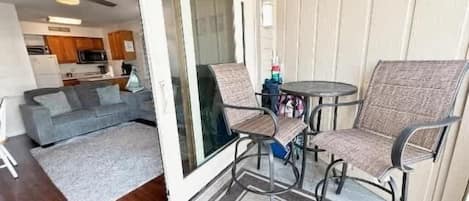 Un patio con puerta corrediza de vidrio que da a una sala de estar, una mesa redonda con sillas y una pequeña cocina visible a través de la puerta.