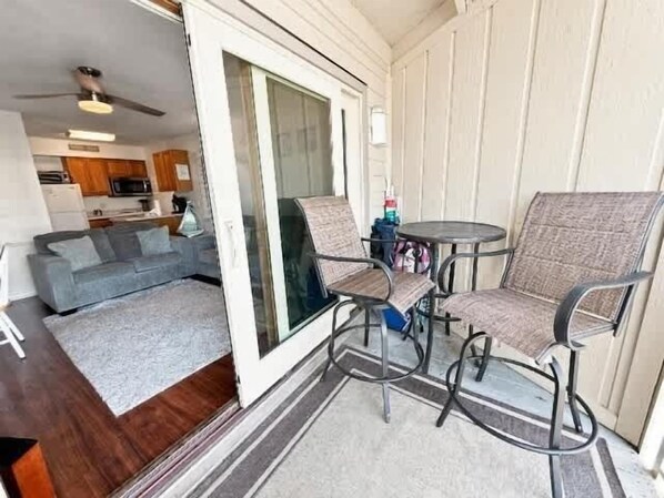 A patio area with a sliding glass door leading to a living room, a round table with chairs, and a small kitchen visible through the door.
