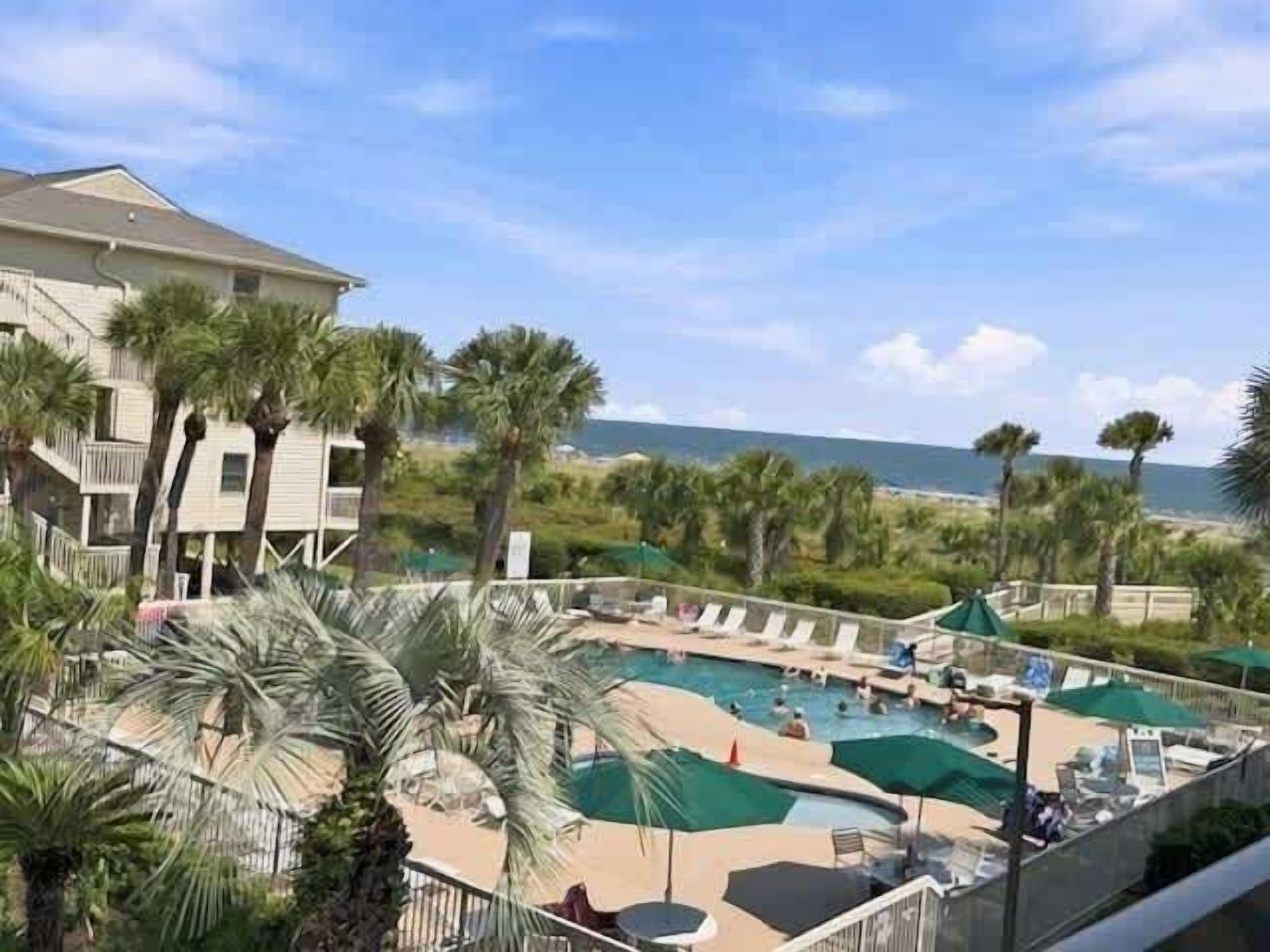 A resort with a pool area, palm trees, and a view of the ocean.